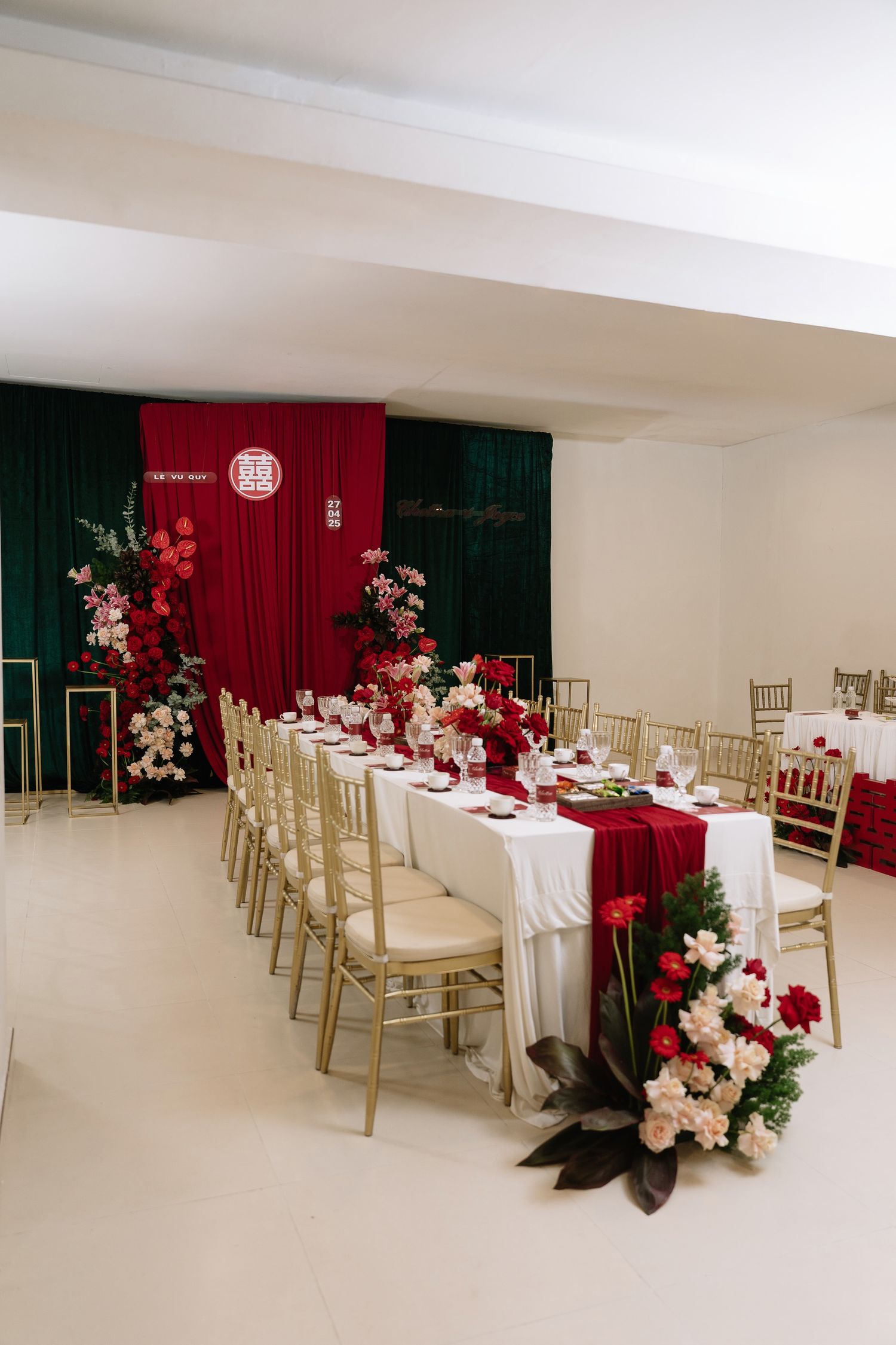 Elegant red and white wedding reception table with gold Chiavari chairs and floral backdrop.