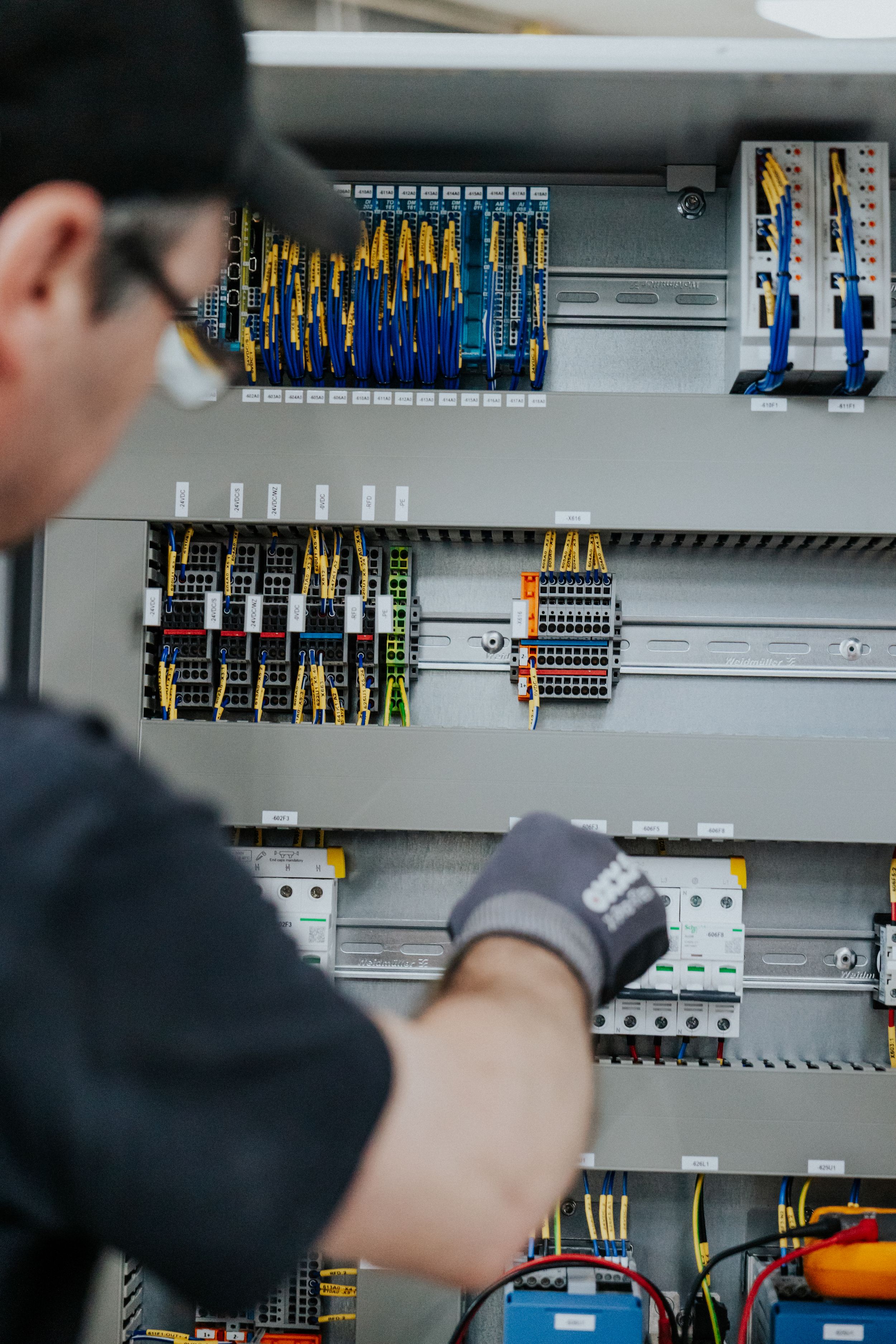 Electrician working on industrial control panel with circuit breakers and wiring.