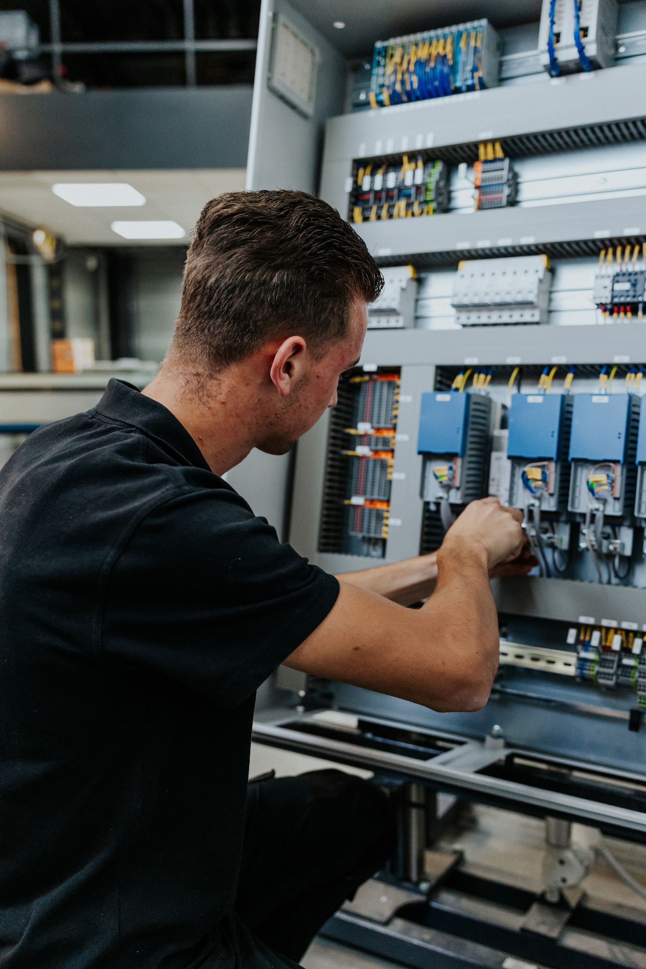 Technician inspecting electrical control panel with circuit breakers and wiring components.