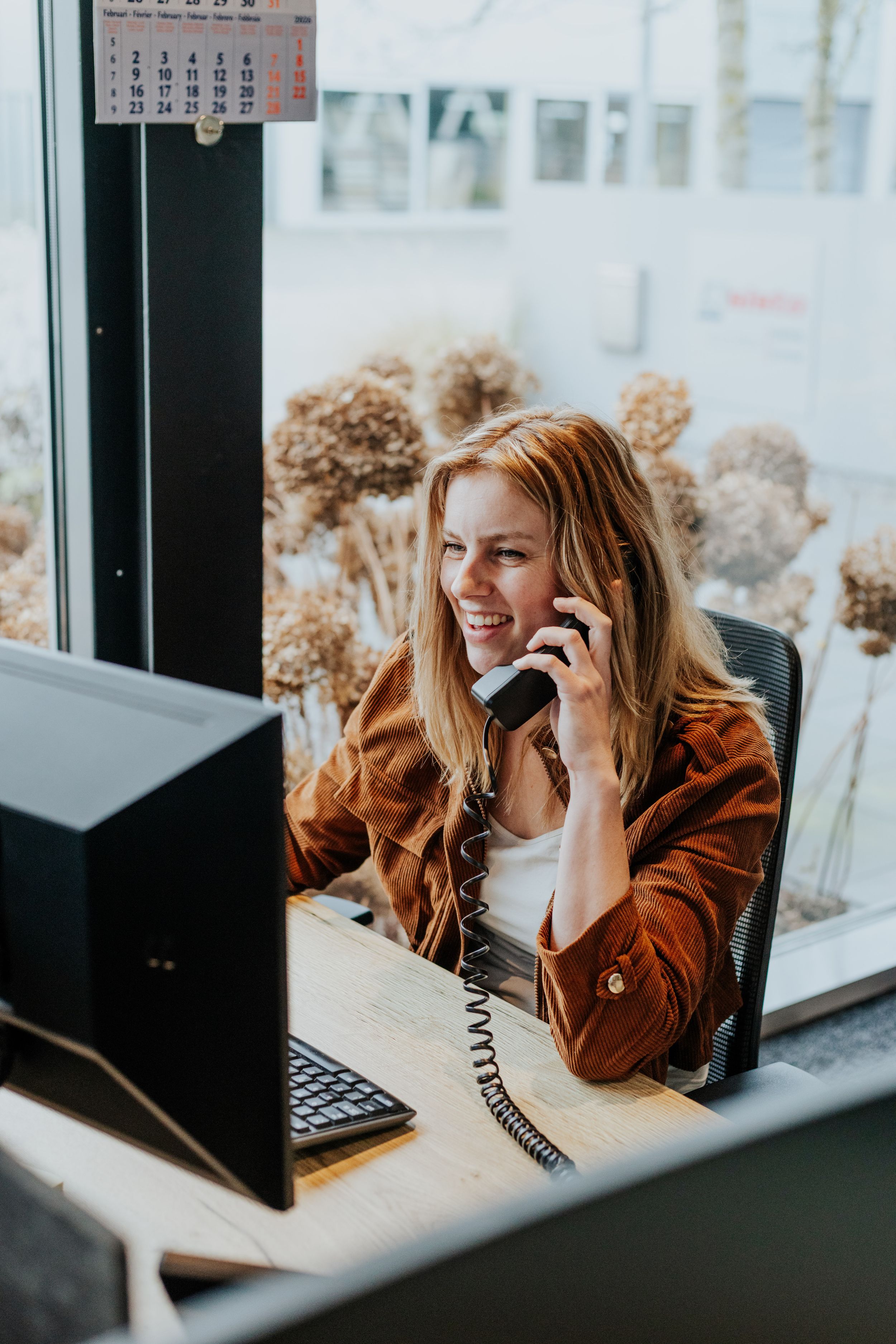 Professional speaking on landline phone while working at desk near window.