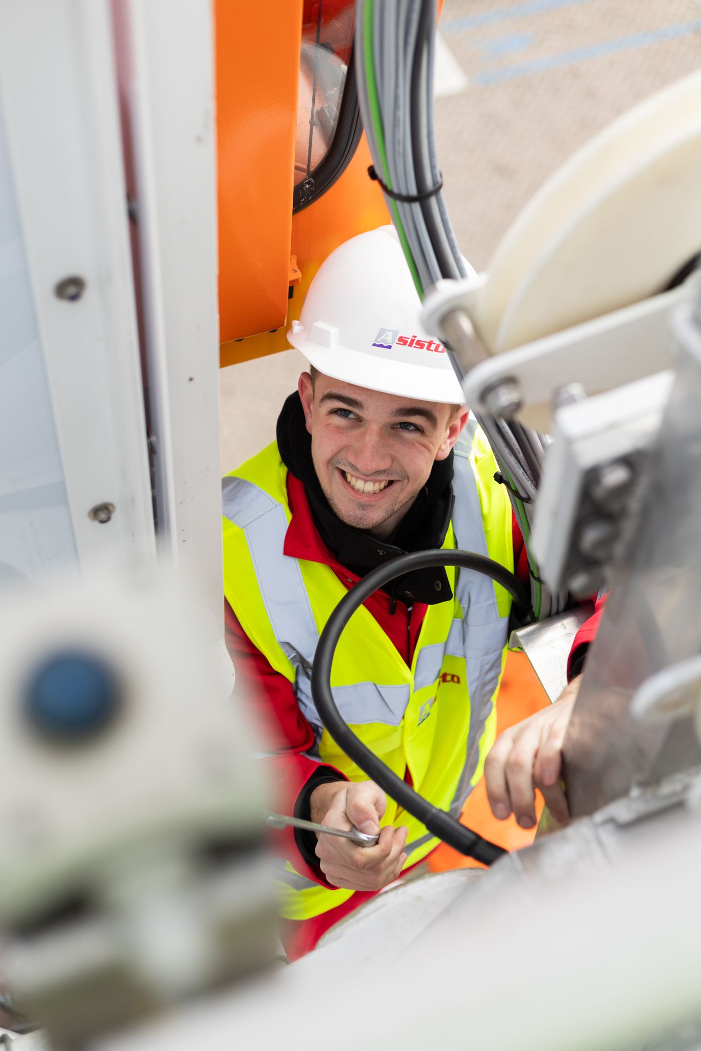 Industrial worker in safety gear and hard hat smiling while inspecting equipment in a manufacturing facility.