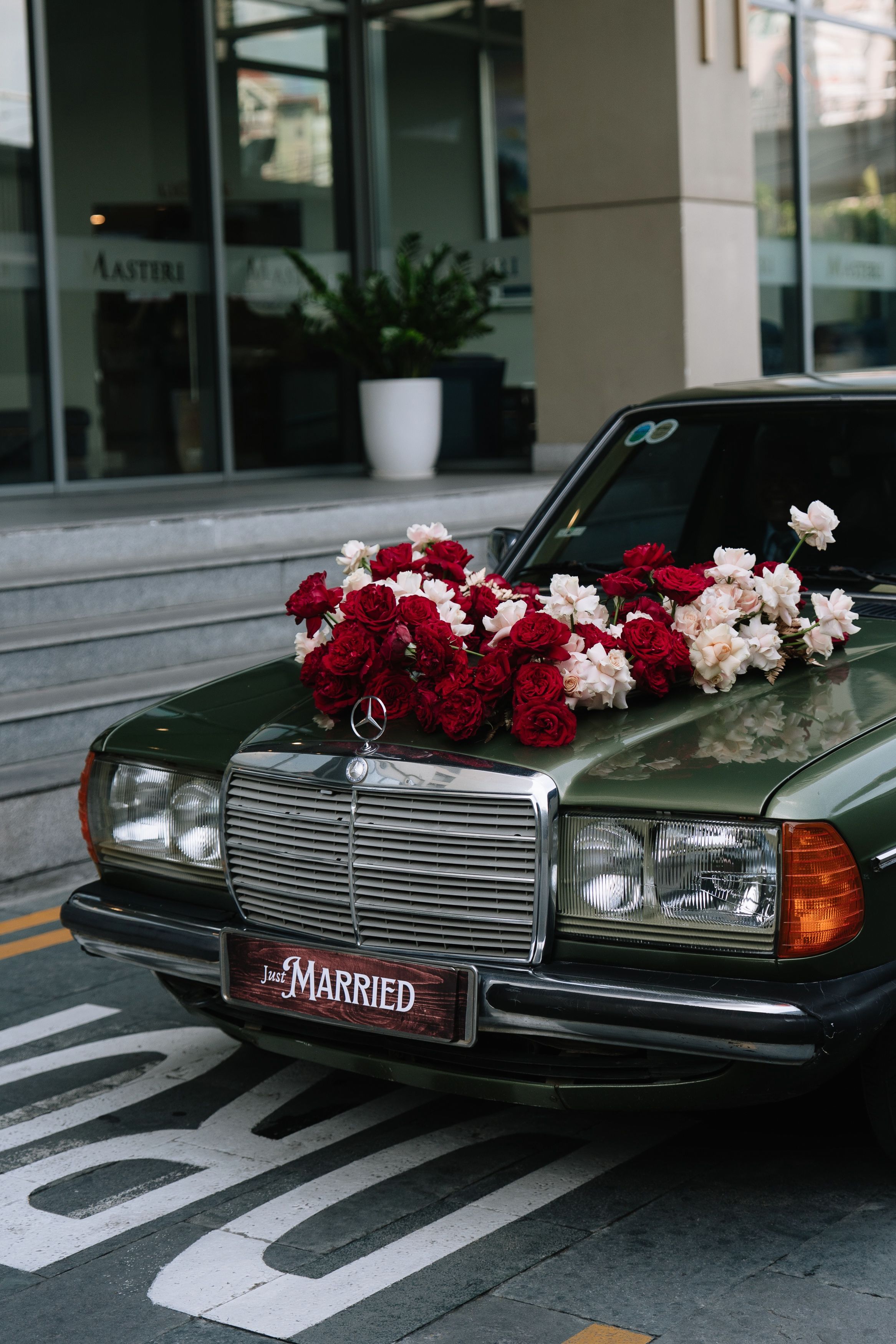 Vintage dark green Mercedes-Benz wedding car decorated with red and white roses and Just Married license plate.