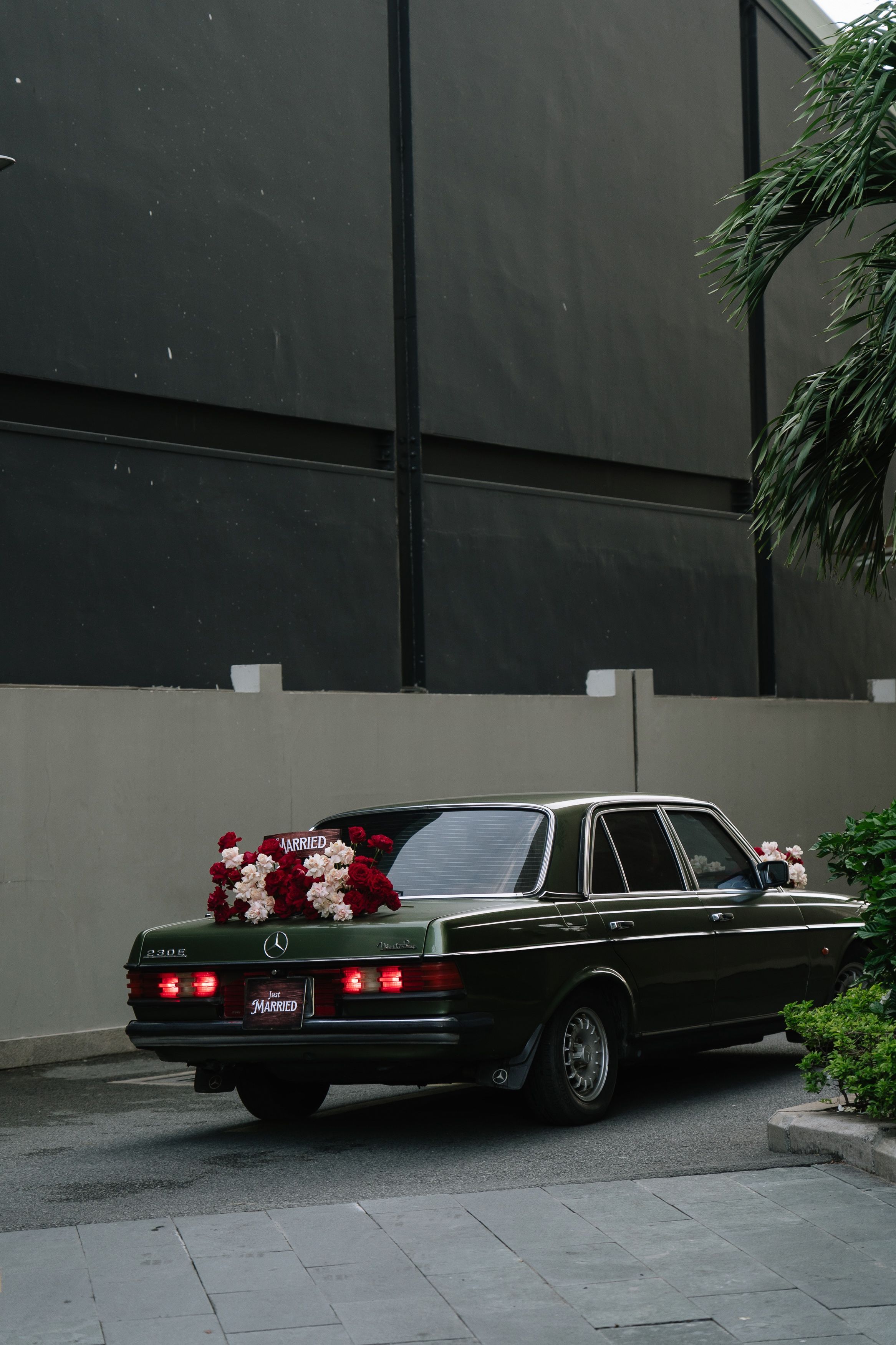 Classic dark green Mercedes-Benz sedan decorated with red and white floral arrangement parked outside wedding venue.