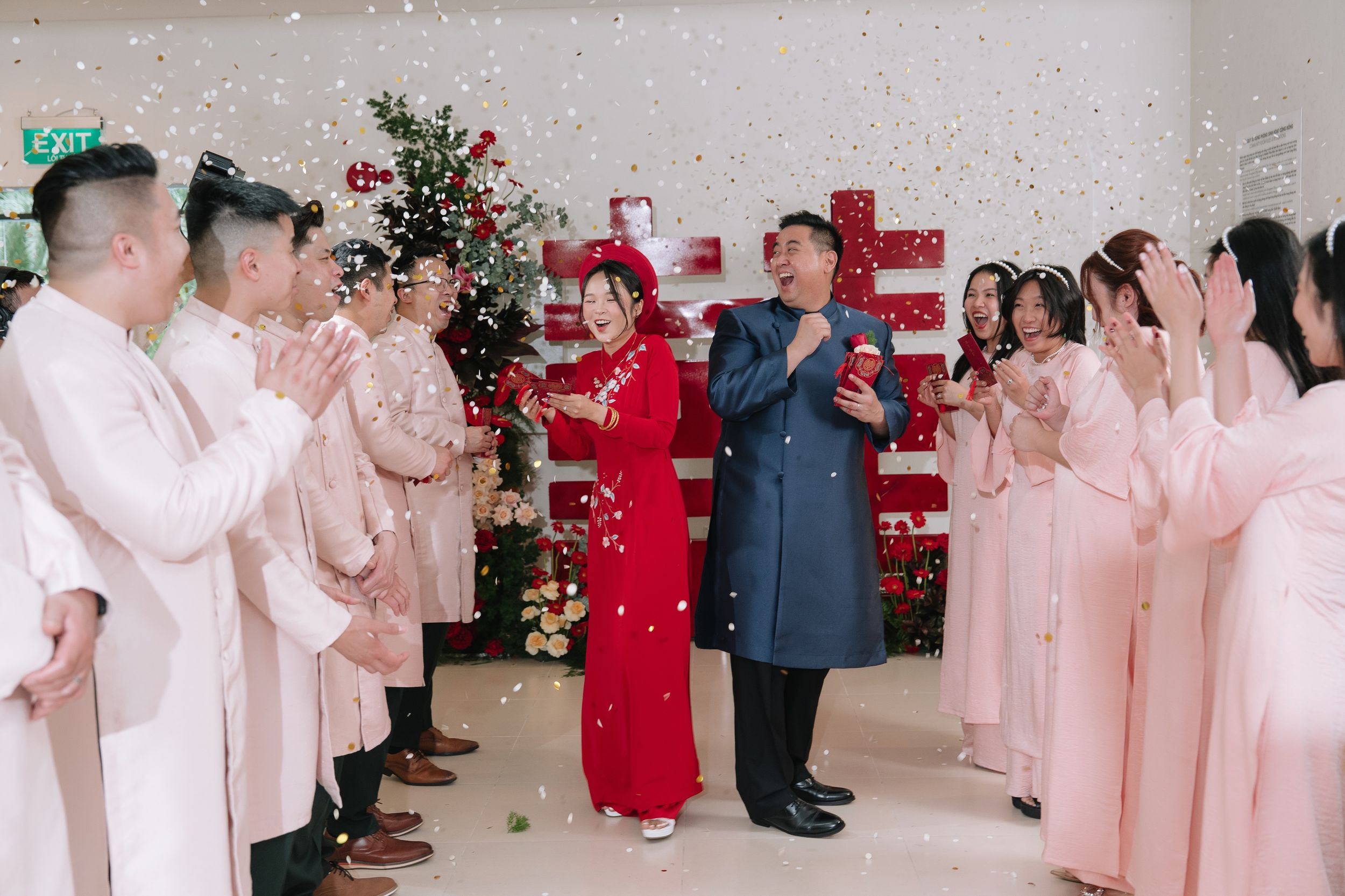 Vietnamese wedding couple in red ao dai and blue suit walking through confetti shower with wedding party.
