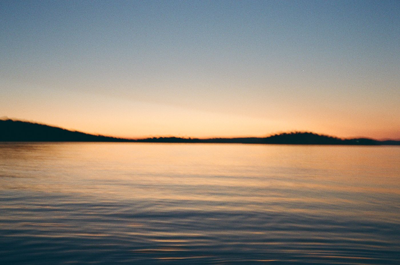 7 panoramic photos of calm ocean waters with soft sunset lighting and distant coastline on the horizon.