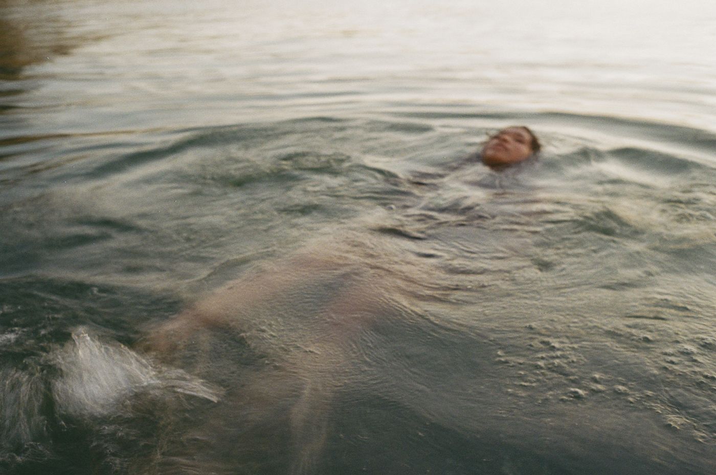 Someone floating peacefully in rippling water at dusk, creating gentle waves on the surface.