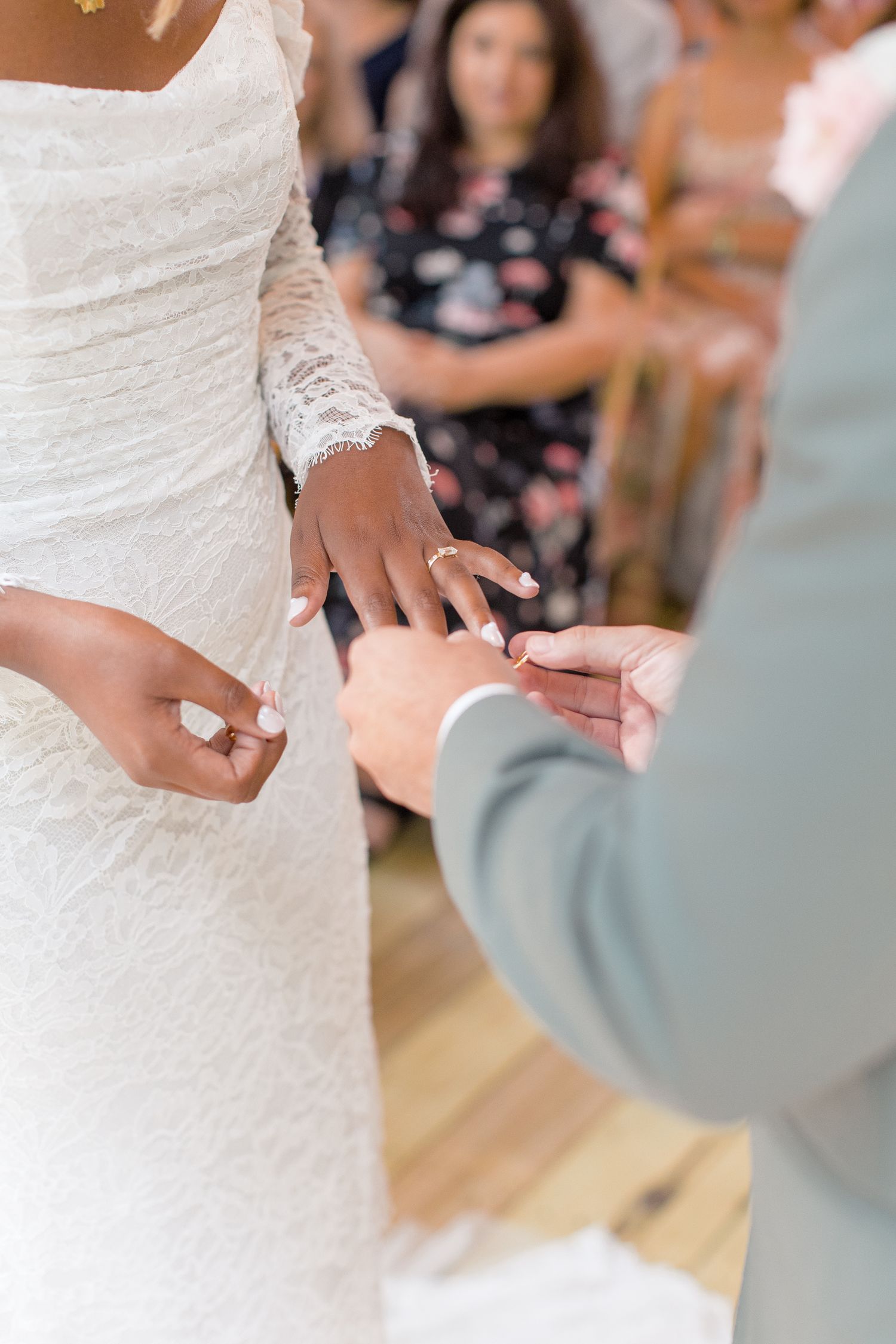 Close-up view of a bride in a white lace wedding dress exchanging rings with the groom during a wedding ceremony.