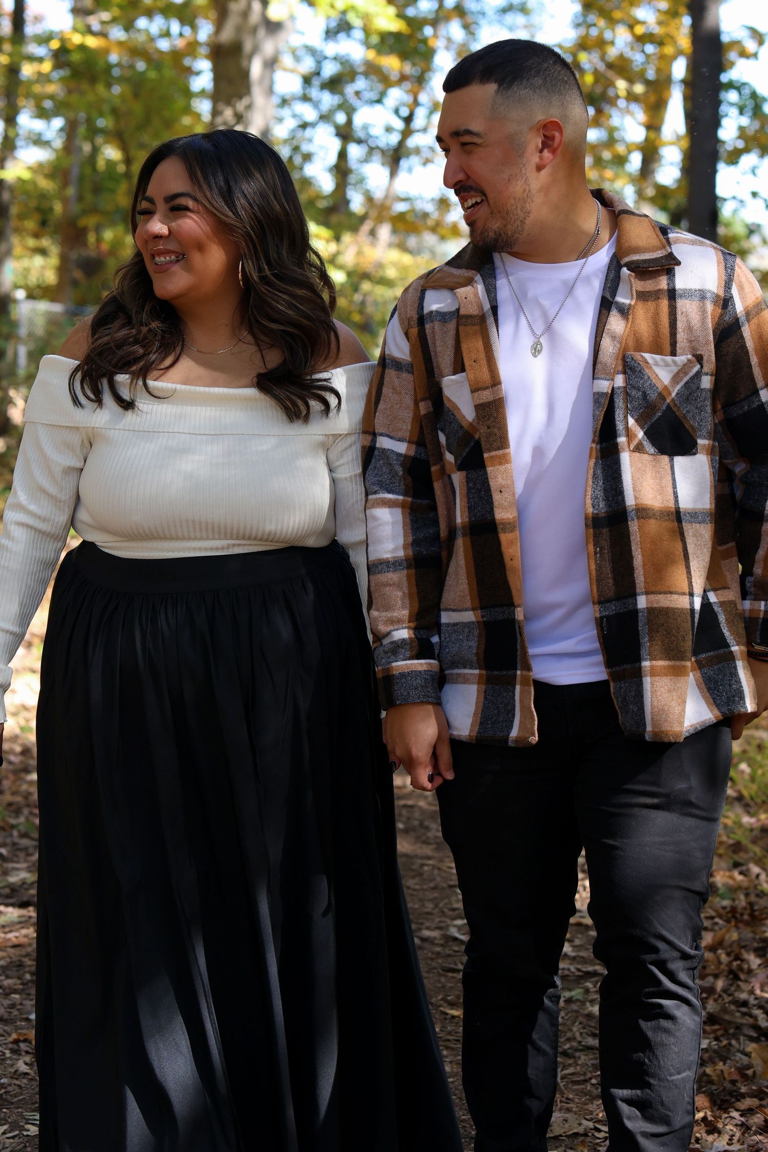 A couple laughs and embraces while posing for outdoor photos in coordinating outfits during an autumn photoshoot.
