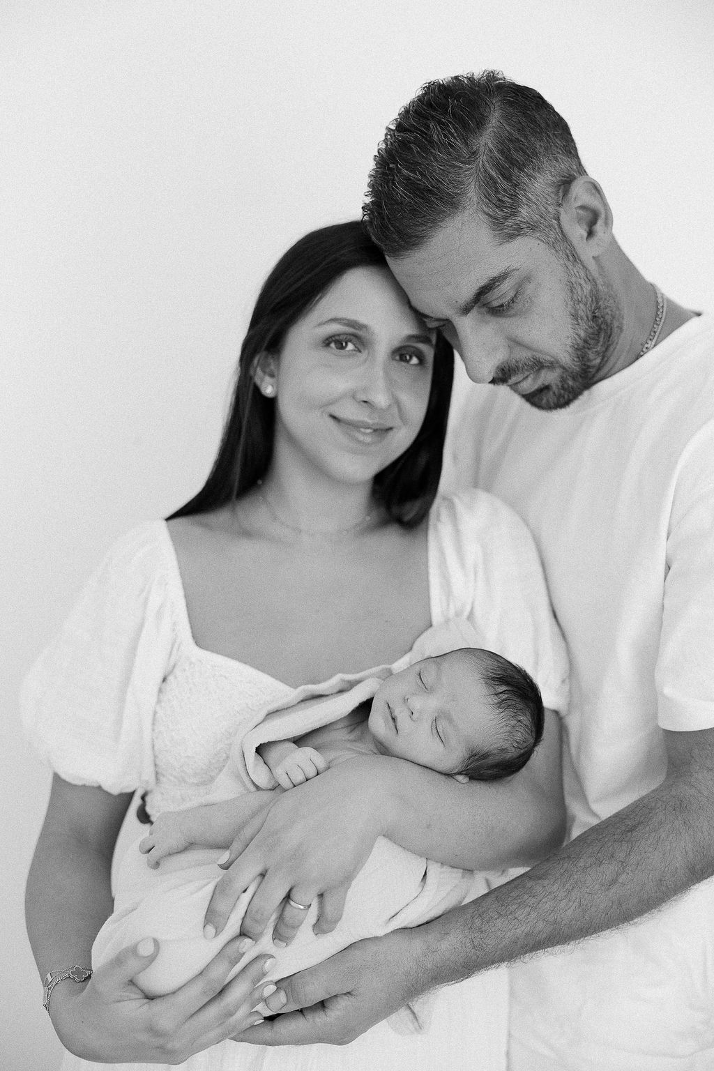 Black and white portrait of parents holding their newborn baby against a plain background.