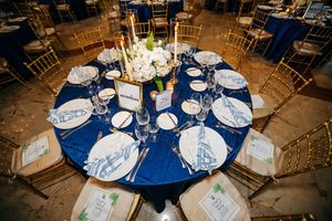 Formal table setting with blue linens, gold chairs, and white floral centerpiece at an elegant event.