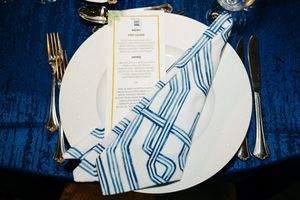 Place setting featuring white plate with blue striped napkin and menu on navy tablecloth.