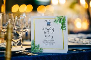 Wedding reception menu card decorated with tropical palm leaves on elegant table setting.
