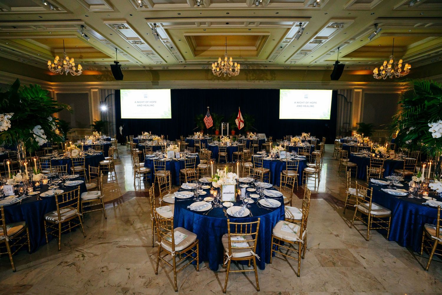 Elegant ballroom setup with navy blue linens, gold chairs, and crystal chandeliers for a formal event reception.