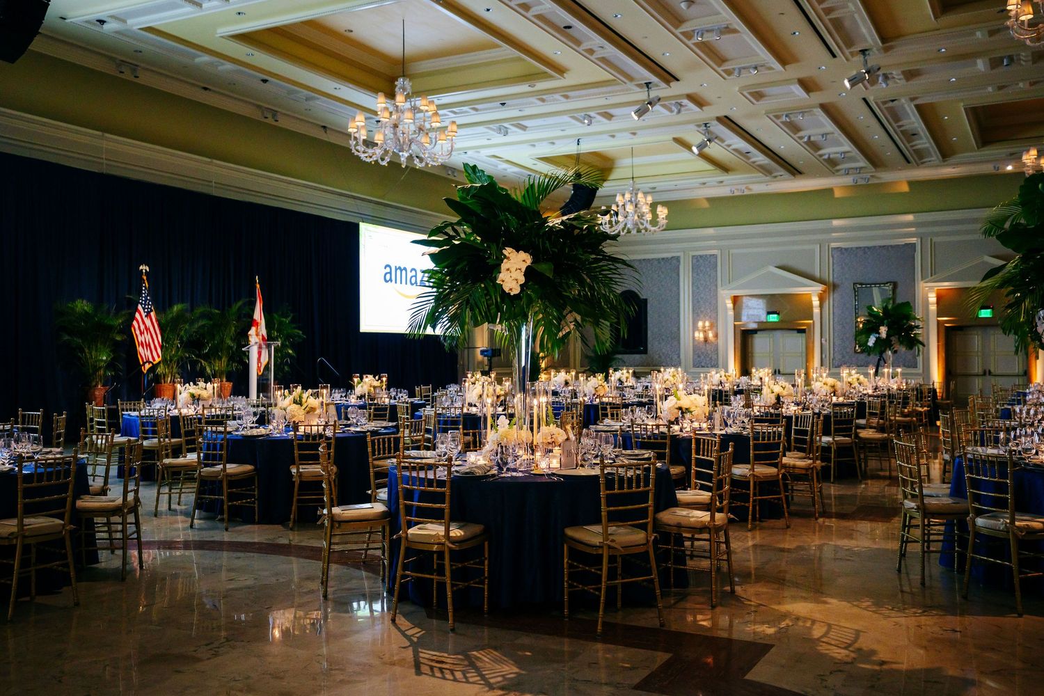 Large elegant banquet hall with wood beamed ceilings, chandeliers, and multiple dining tables set for an event.
