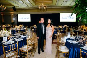 Elegant ballroom reception setup with navy blue linens, gold chairs and illuminated screens.