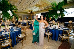 Two guests pose in formal attire against a backdrop of elegant table settings and tropical decor.
