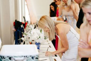 People signing guest books at an elegant event with white floral centerpieces on tables.