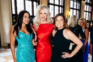 Three women in evening gowns pose together at a formal event.