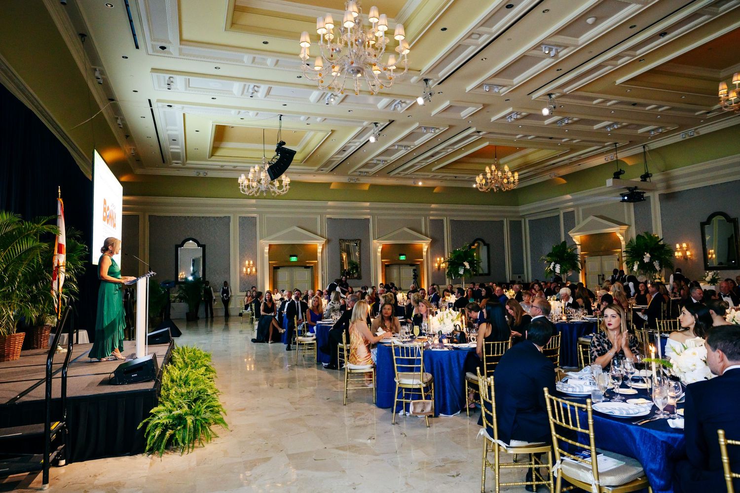Elegant ballroom filled with guests at round tables under crystal chandeliers during a formal banquet event.