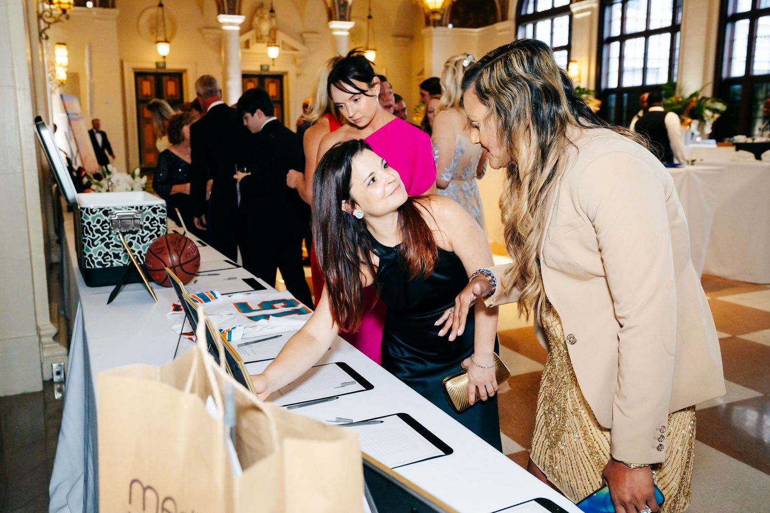 Attendees engage with a vendor at a bright indoor event space with elegant lighting and window views.