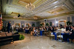 Elegant ballroom filled with guests at round tables under ornate chandeliers during a formal event.