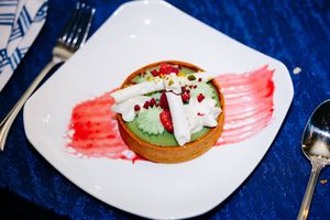 Artfully plated dessert with white cream and red sauce on square white plate with blue tablecloth.