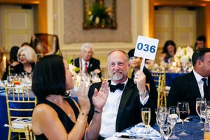 Formal gala attendee holding up bidding paddle number 036 during auction event.