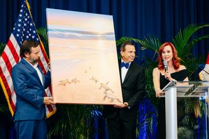 An art piece featuring a beach landscape scene being presented on stage with American flag.