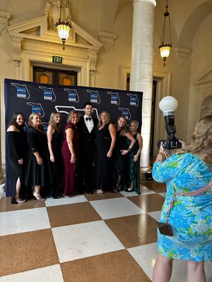 Group photo being taken against branded backdrop at formal event in elegant venue hallway.
