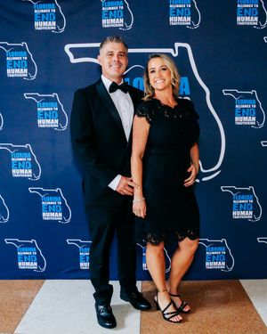 Couple in formal wear poses against backdrop with Florida outline at black-tie event.