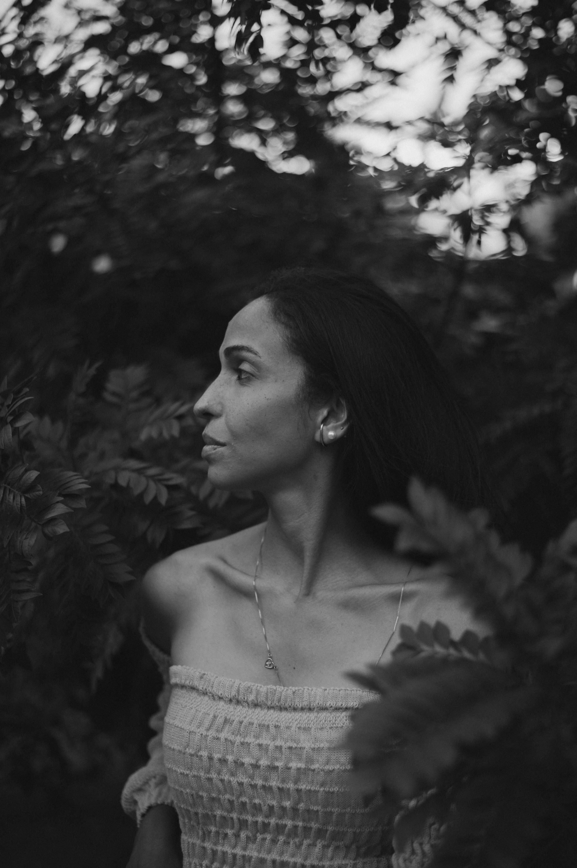 Dramatic black and white portrait of a person in an off-shoulder top surrounded by foliage.