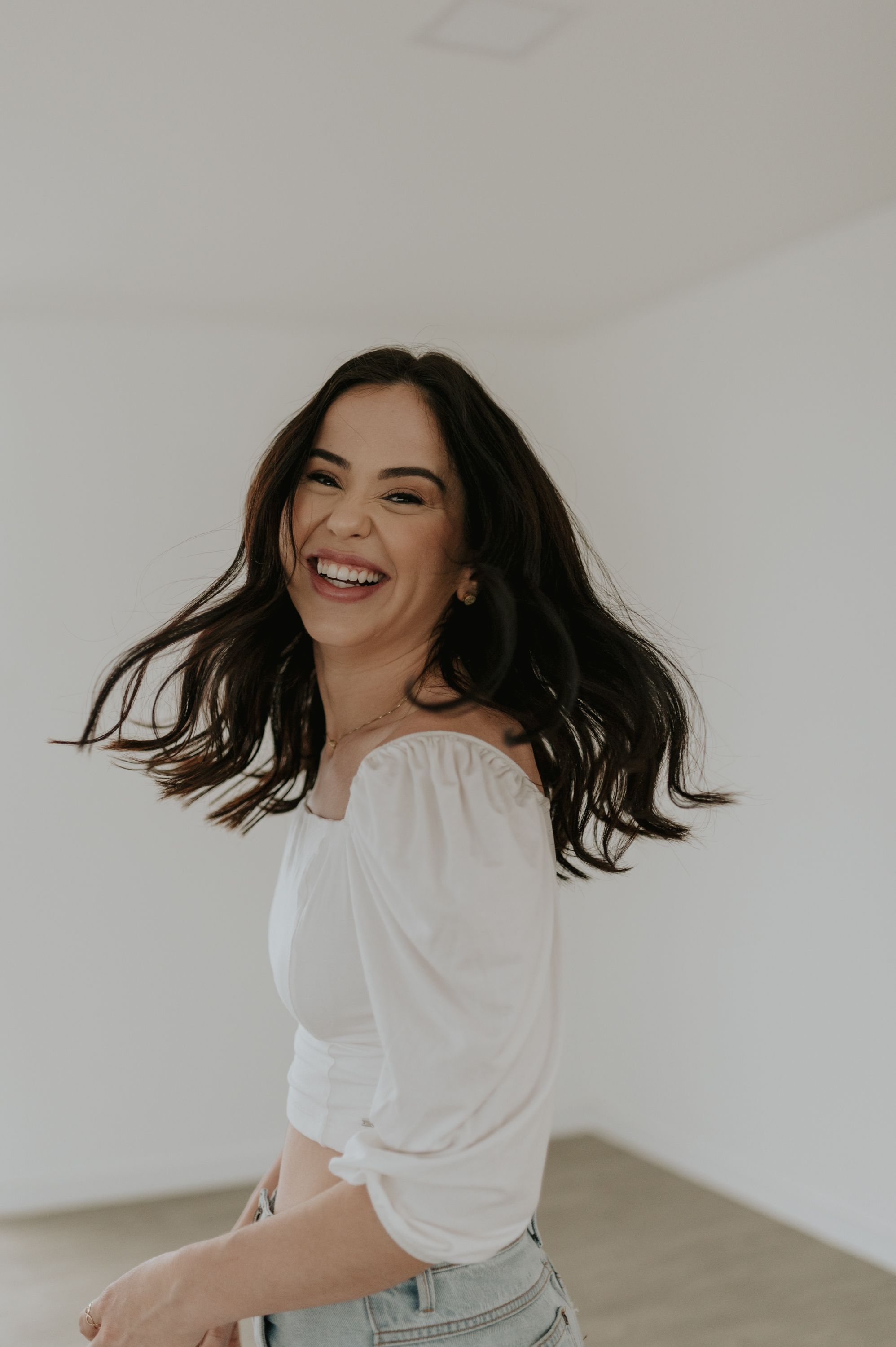 Candid portrait of a person in white top and jeans laughing with hair in motion.