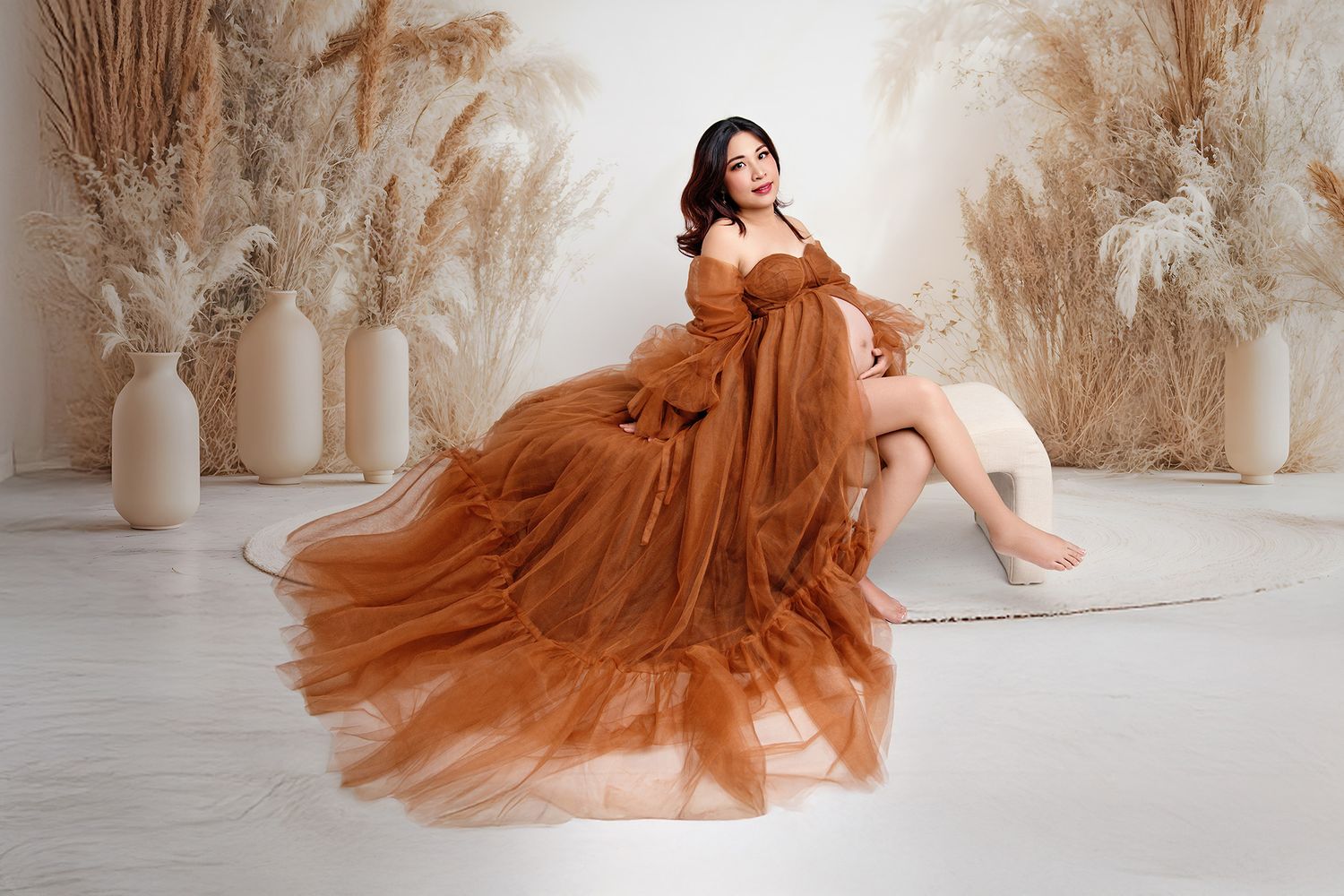 Maternity photoshoot in flowing rust-colored dress with pampas grass backdrop.