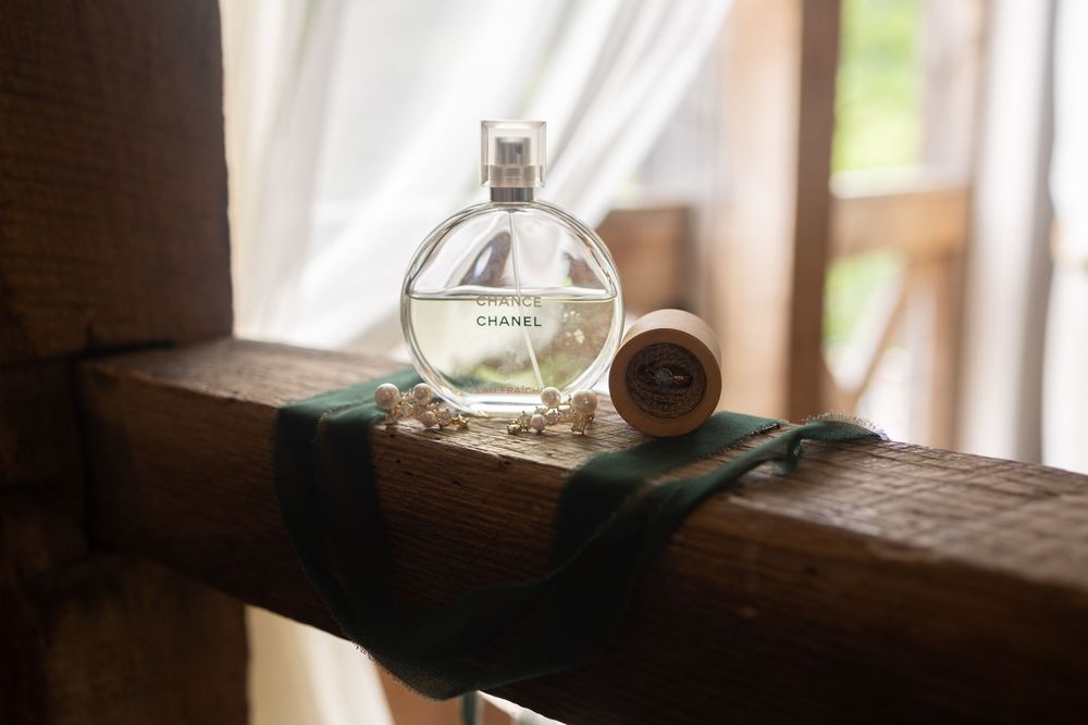 Chanel Chance perfume bottle displayed on rustic wooden beam with pearl bracelet and ribbon.
