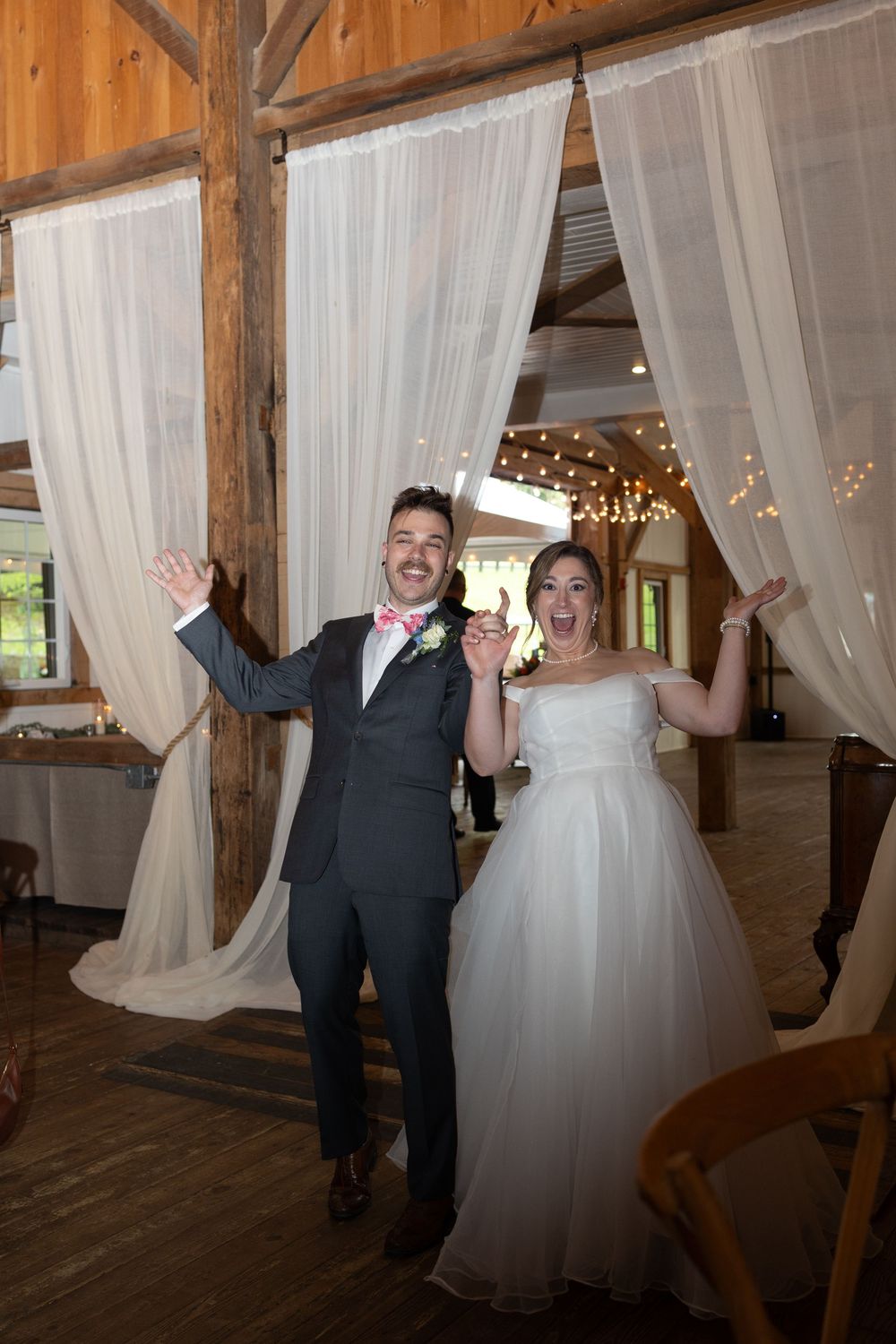 Excited bride and groom make grand entrance into rustic barn wedding reception venue.