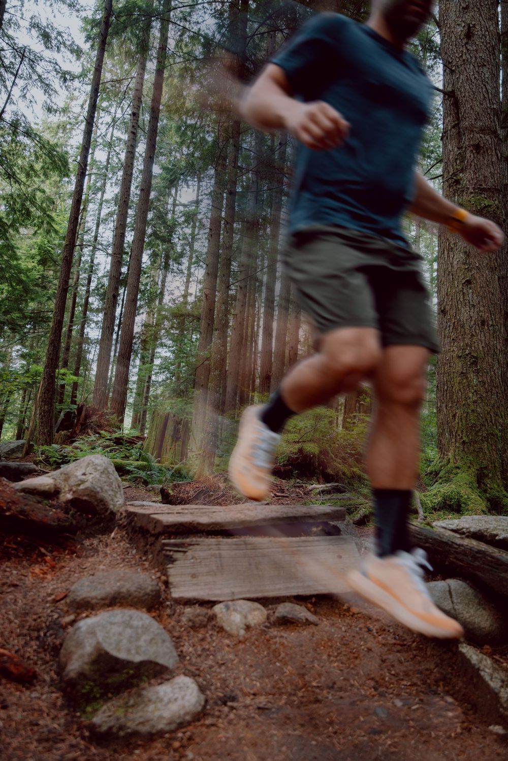 Motion blur sequence of trail runner jumping over rocks on forest path.