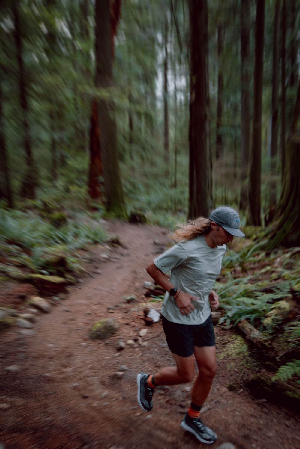 Motion-blurred sequence shows a trail runner navigating through a lush forest path with tall evergreen trees.