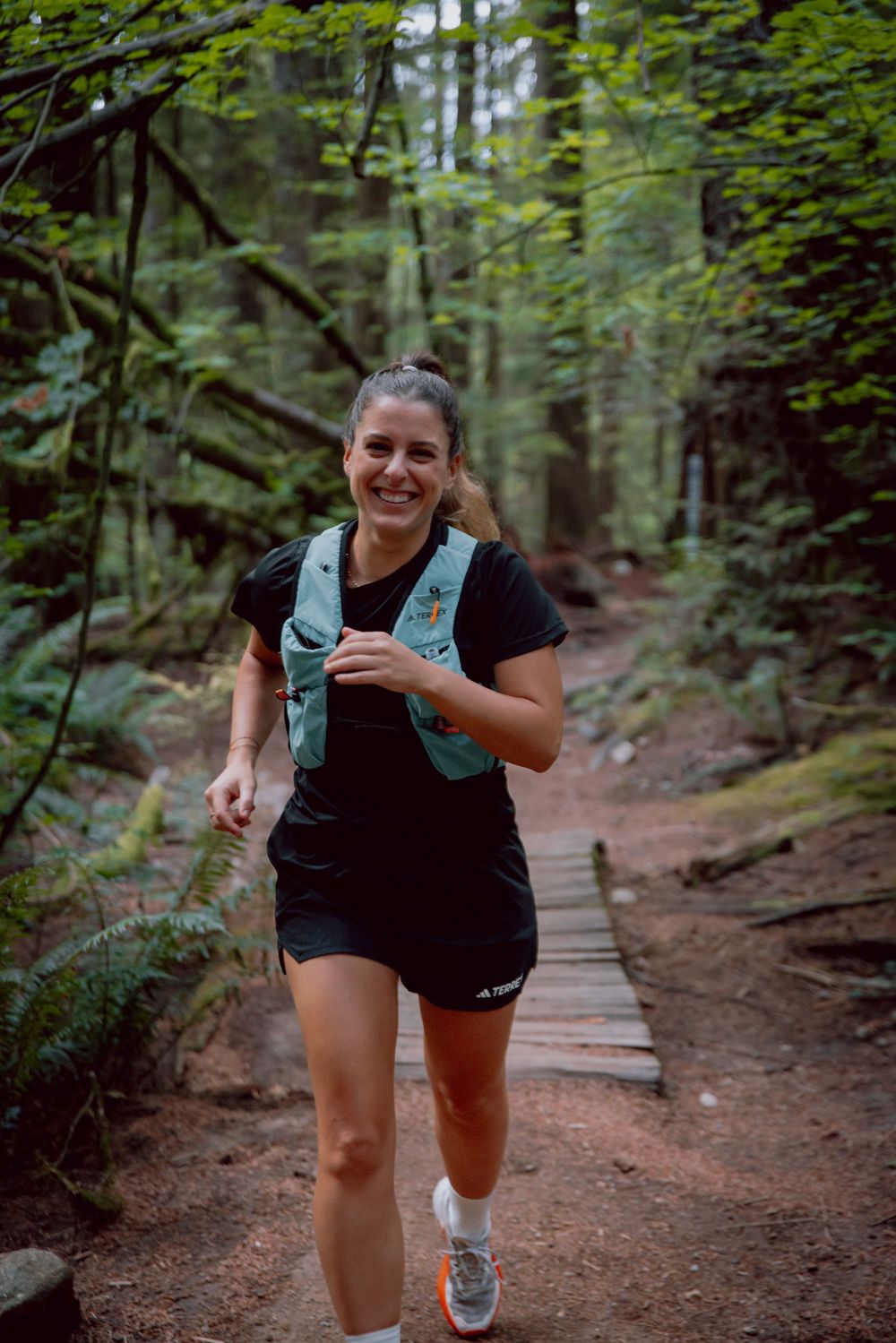 Runner in black athletic wear smiling while running on a forest trail on a summer day.