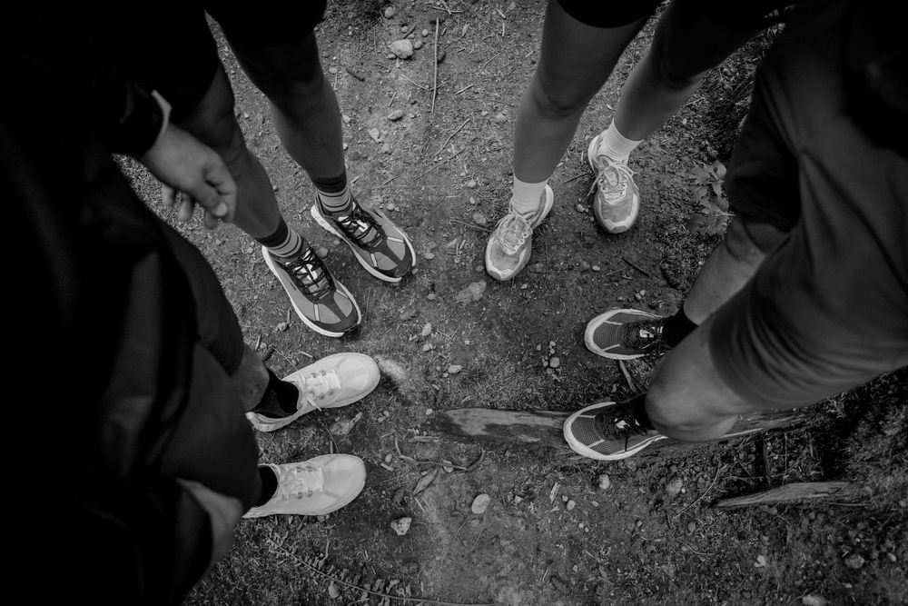 Black and white overhead view of people standing in a circle wearing various casual sneakers and shoes.