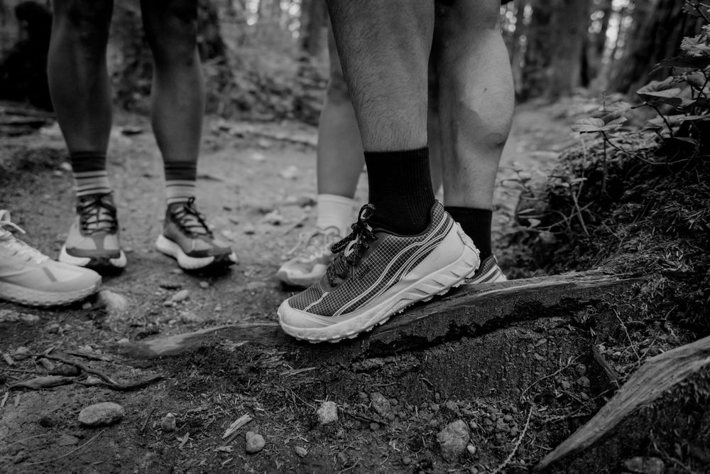 Black and white close-up of hiking shoes on forest trail with legs visible in the frame.