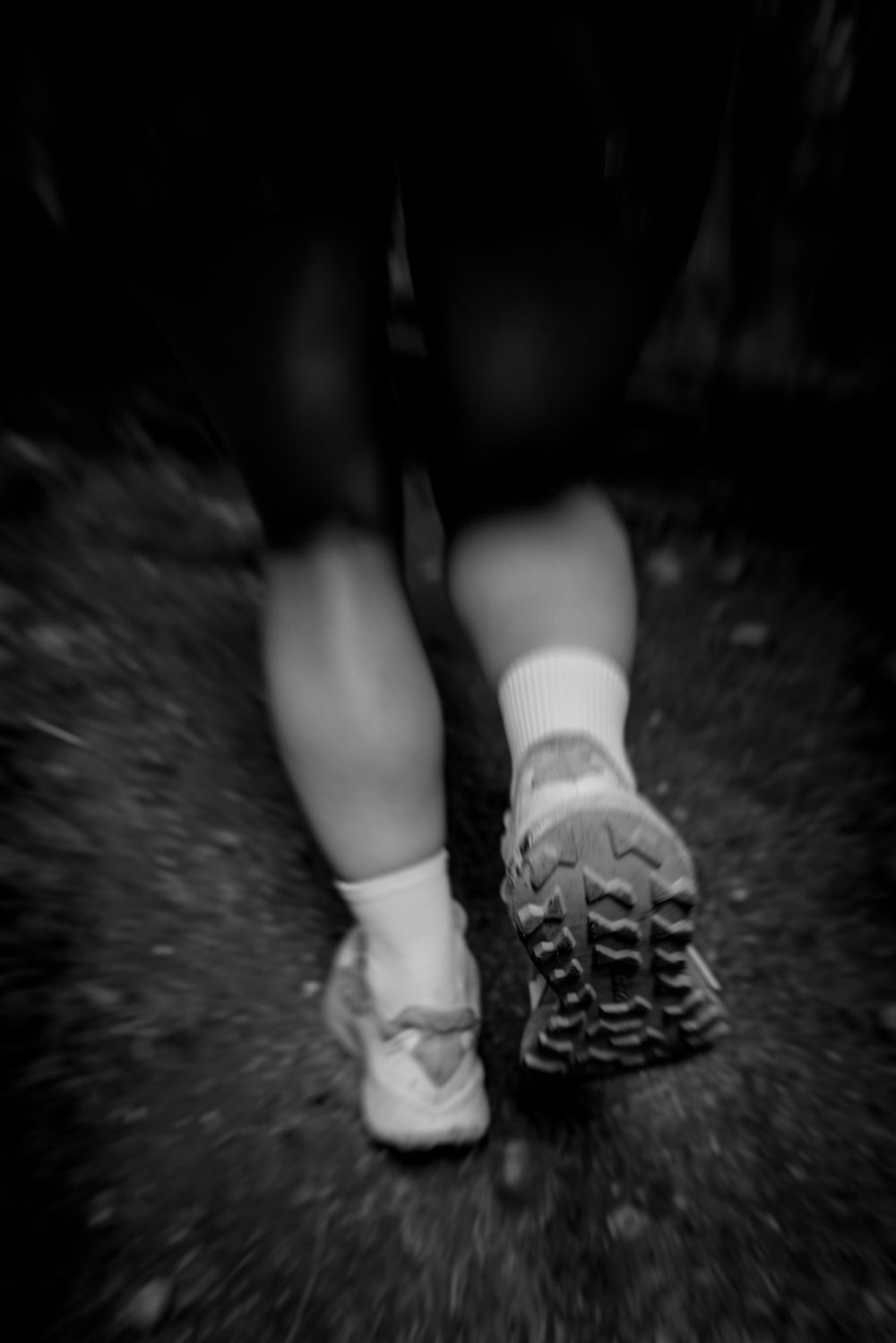Black and white shot of feet walking on a forest trail with zoomed motion blur effect.