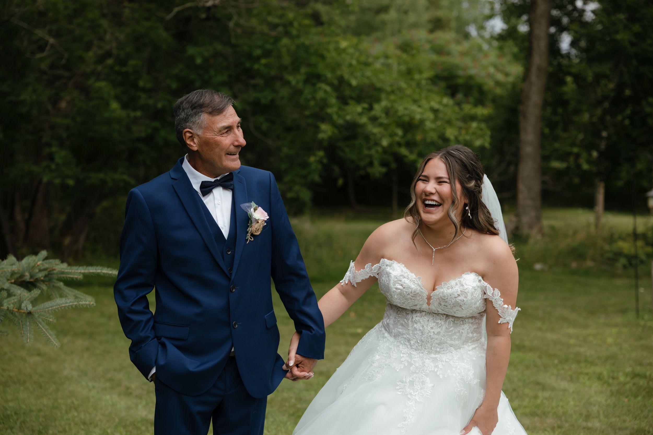 A couple shares a joyful moment outdoors at their wedding, with the bride in white and groom in navy blue.