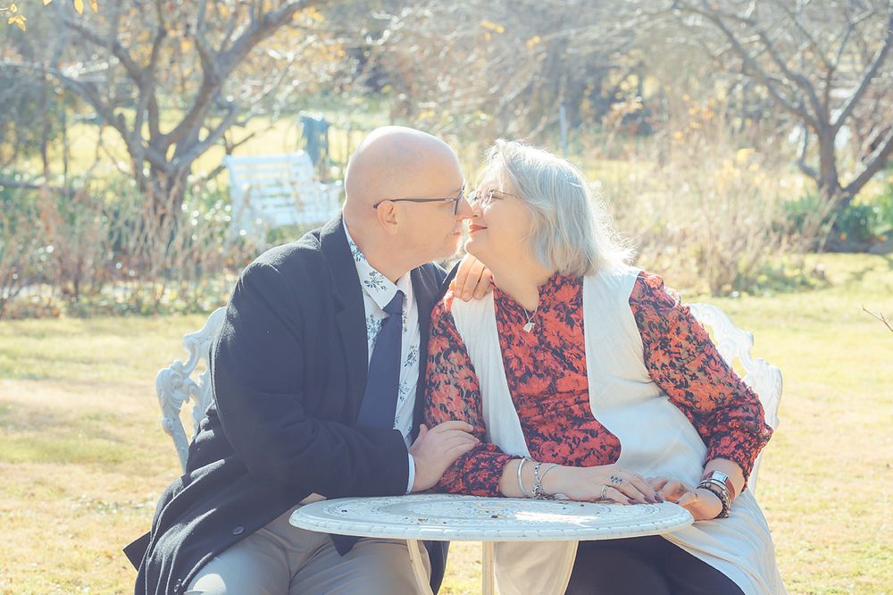 A couple in formal attire sharing sweet kisses in nature during a romantic outdoor photoshoot.