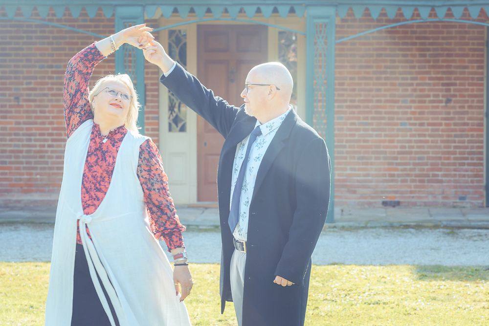 Two people standing outdoors in front of a brick building while engaged in conversation.