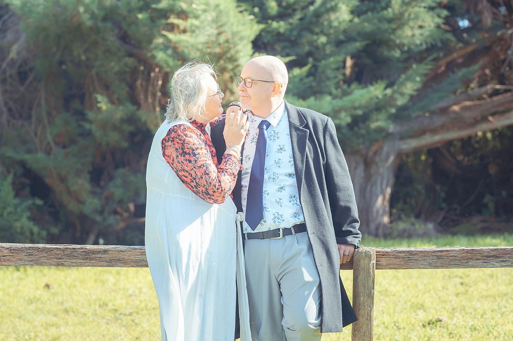 Senior couple walking hand in hand through a lush green park during a sunny day.