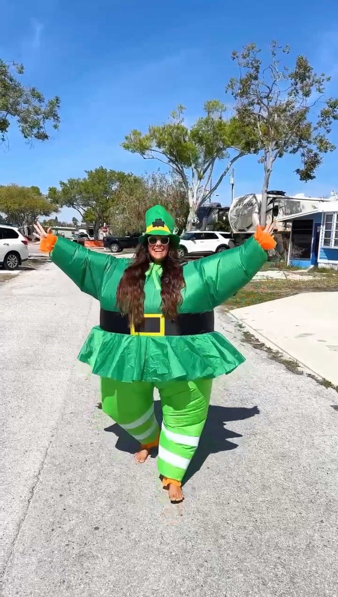 Woman in inflatable St. Patrick's Day leprechaun costume posing outdoors in RV park.