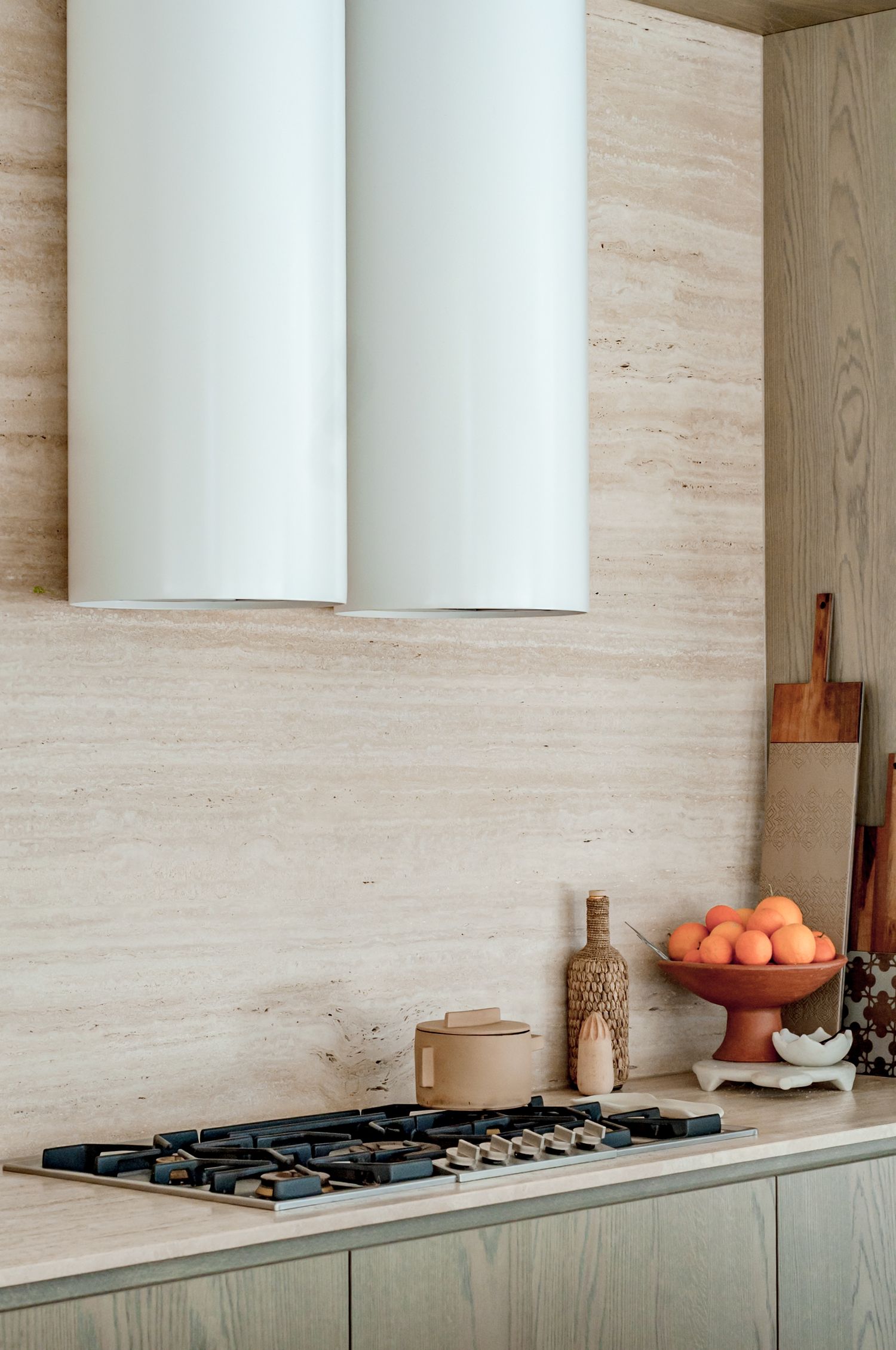 Modern kitchen with white cylindrical range hood, wood paneling, and oranges in a terracotta bowl on the counter.