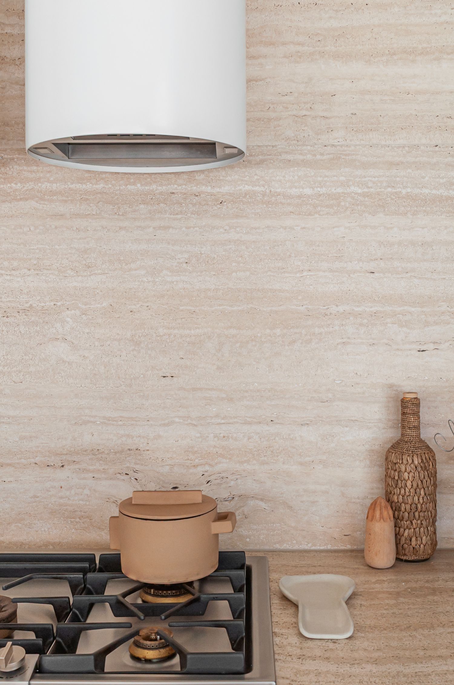 Modern kitchen interior with minimalist clay pots and cookware on gas stovetop against textured beige stone wall.
