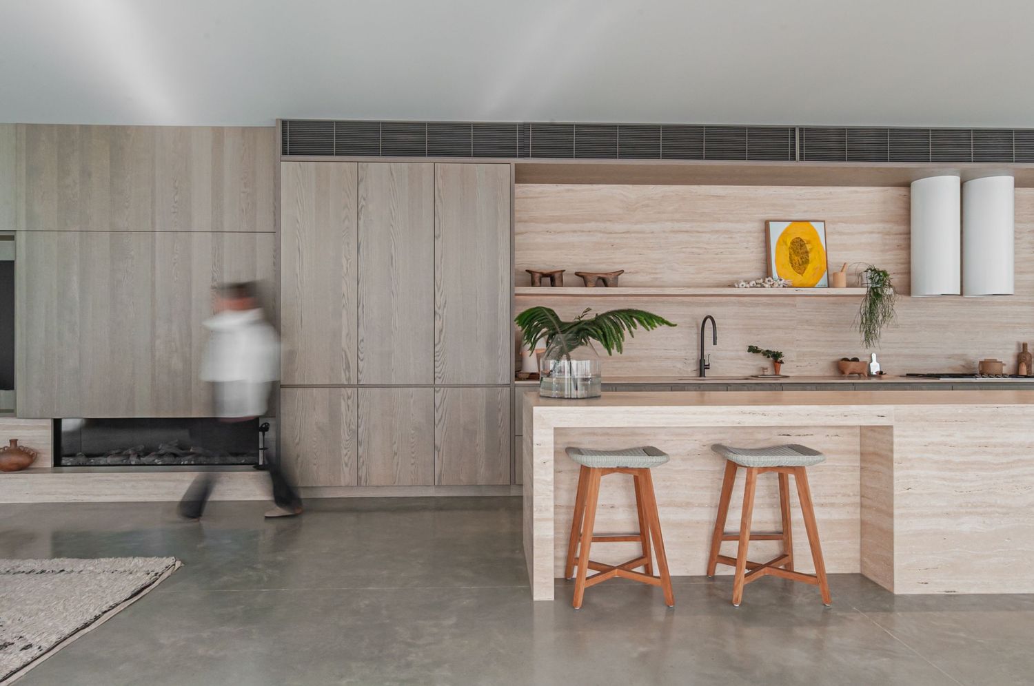 A modern white kitchen and dining space with light wood cabinets, bar stools, and elegant pendant lighting.