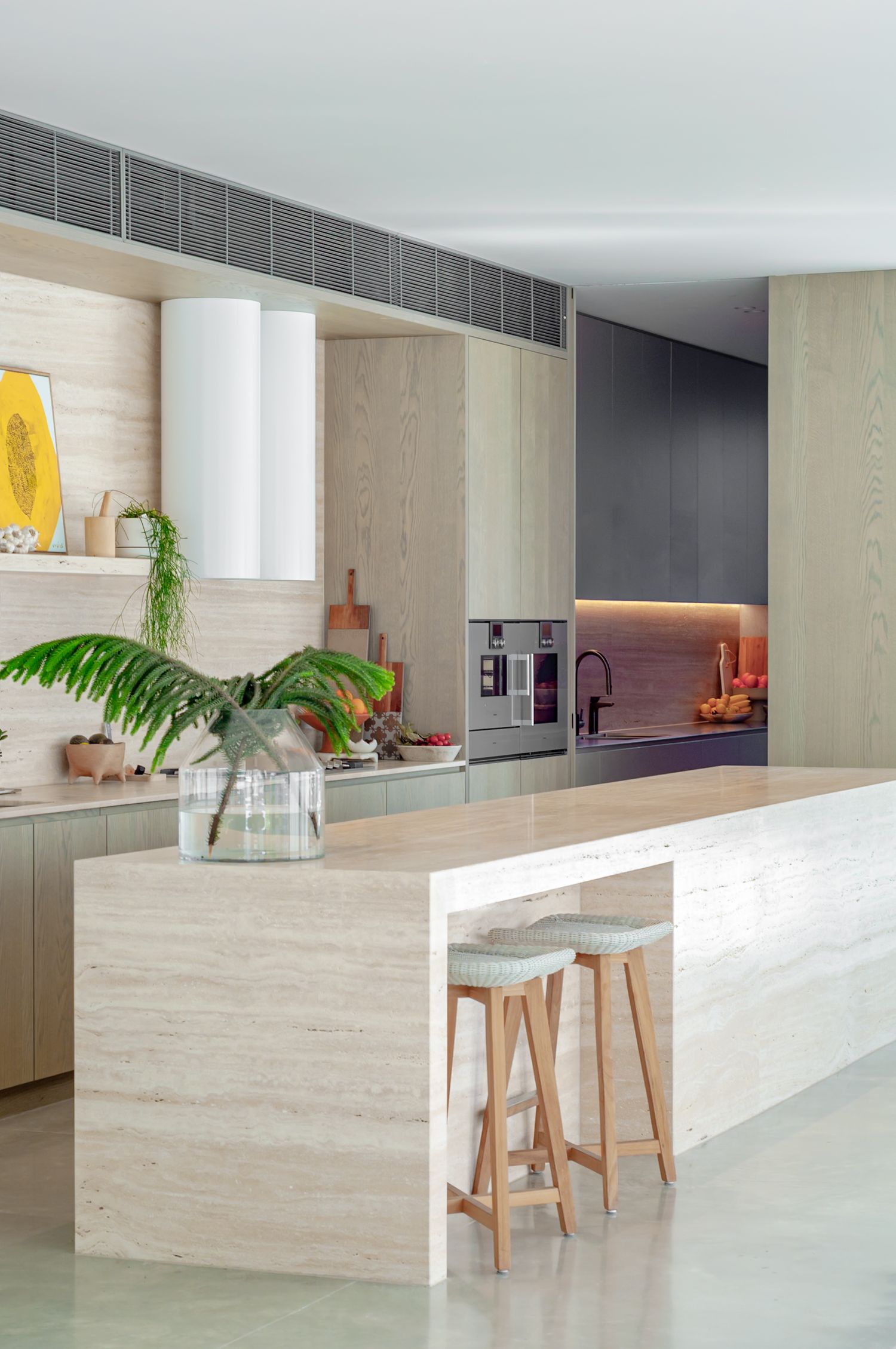 Modern minimalist kitchen featuring light wood cabinetry, white island with bar stools, and tropical plant decor.